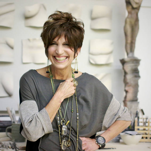 Sculptor Tanya Ragir smiling in her studio with her artwork behind her